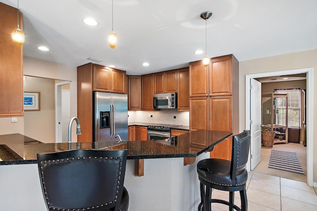 kitchen with kitchen peninsula, hanging light fixtures, a breakfast bar area, appliances with stainless steel finishes, and light tile patterned floors