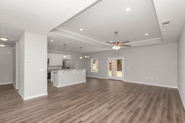 unfurnished living room featuring ceiling fan, a textured ceiling, a raised ceiling, and dark wood-type flooring