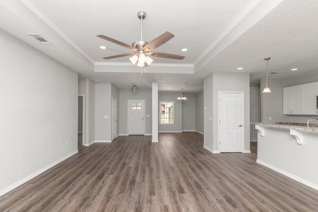 unfurnished living room with crown molding, a tray ceiling, and dark wood-type flooring