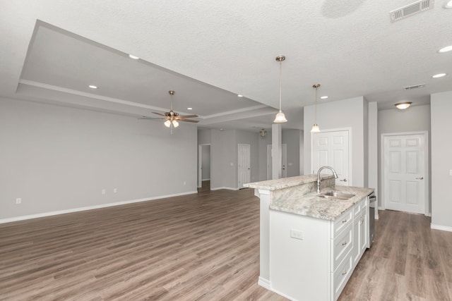 kitchen with white cabinets, decorative light fixtures, hardwood / wood-style flooring, a center island with sink, and sink