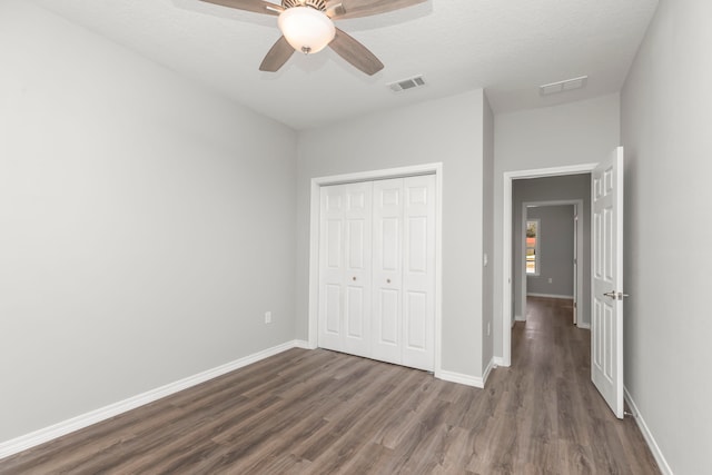 unfurnished bedroom featuring a textured ceiling, dark hardwood / wood-style flooring, ceiling fan, and a closet