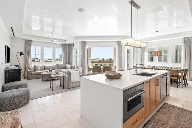 kitchen featuring pendant lighting, sink, ceiling fan with notable chandelier, stainless steel appliances, and a kitchen island with sink