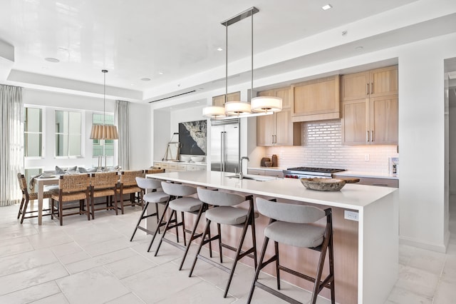 kitchen with a breakfast bar area, decorative light fixtures, a raised ceiling, and an island with sink