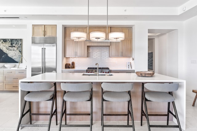 kitchen with a center island with sink, hanging light fixtures, built in fridge, and light tile floors