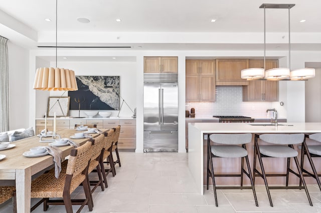 kitchen with stainless steel built in refrigerator, pendant lighting, light tile flooring, sink, and an island with sink