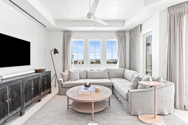 tiled living room with ceiling fan and a tray ceiling