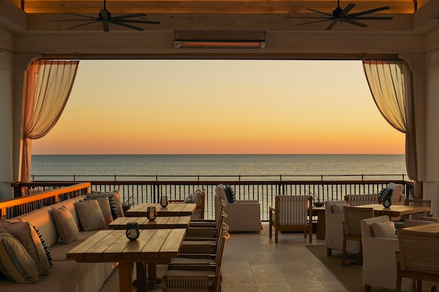 patio terrace at dusk featuring a water view, ceiling fan, and a balcony