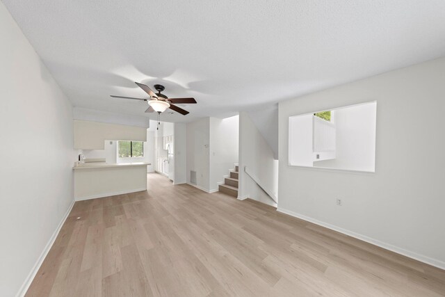 unfurnished living room featuring ceiling fan, light wood-type flooring, and a textured ceiling