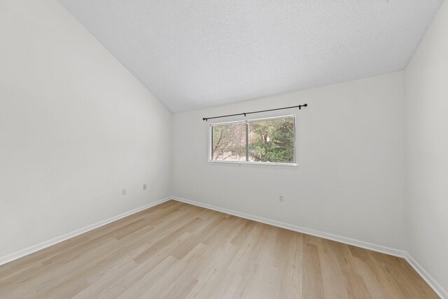 empty room featuring a textured ceiling, light hardwood / wood-style floors, and vaulted ceiling