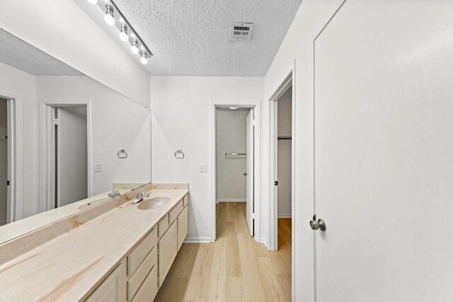 bathroom with a textured ceiling, wood-type flooring, track lighting, and large vanity