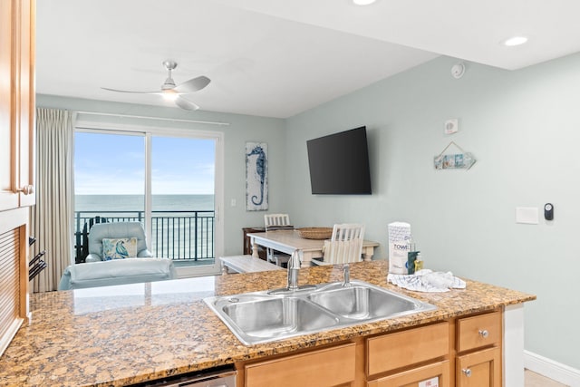 kitchen featuring light stone countertops, light brown cabinets, a water view, sink, and ceiling fan