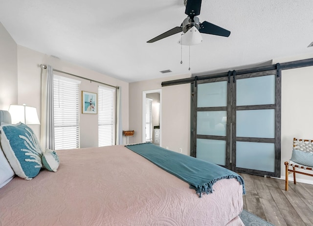 bedroom featuring a barn door, ceiling fan, and hardwood / wood-style floors