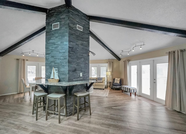 dining area with beamed ceiling, wood-type flooring, track lighting, and a healthy amount of sunlight