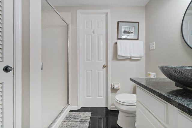 bathroom featuring tile flooring, toilet, large vanity, and a shower with shower door