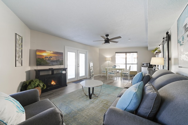 living room featuring french doors, a barn door, ceiling fan, a textured ceiling, and dark wood-type flooring