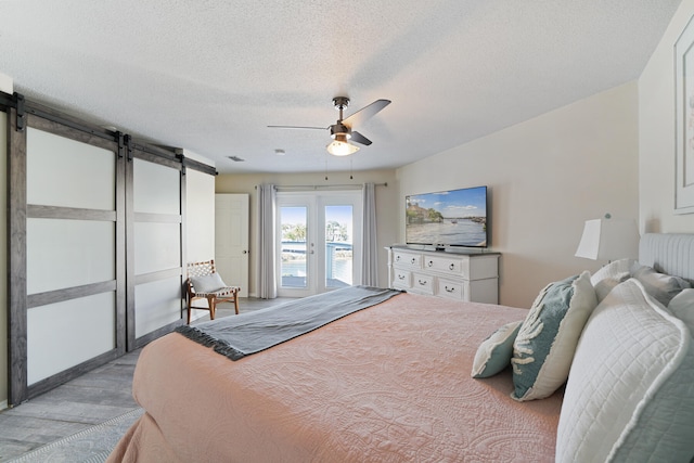 bedroom with a textured ceiling, ceiling fan, light hardwood / wood-style floors, and a barn door