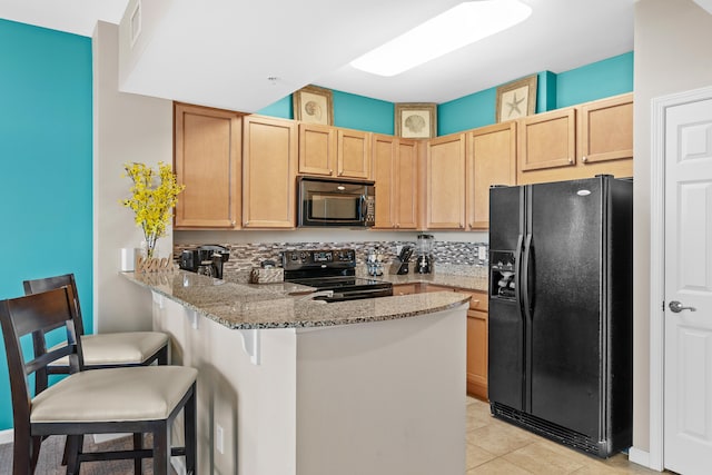 kitchen featuring light tile flooring, tasteful backsplash, a breakfast bar area, black appliances, and light stone countertops