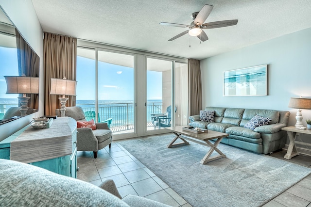 tiled living room with ceiling fan, a water view, and a textured ceiling