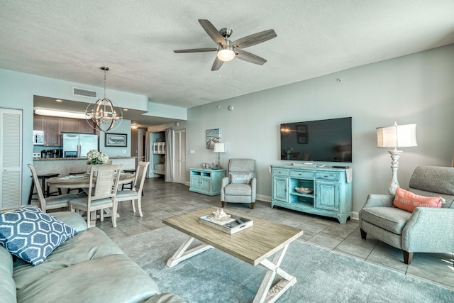 tiled living room with ceiling fan with notable chandelier and a textured ceiling