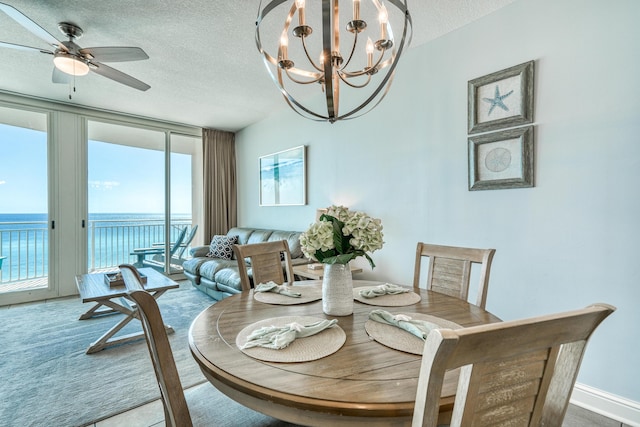 dining space featuring ceiling fan with notable chandelier, a textured ceiling, and a water view