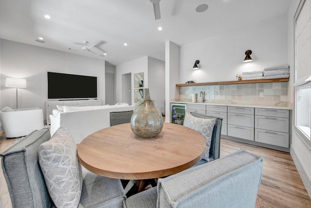 dining room featuring wine cooler, sink, lofted ceiling, and light wood-type flooring