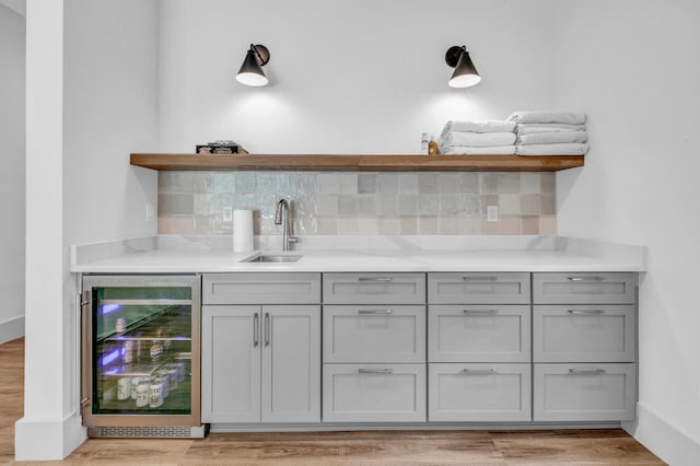 bar with beverage cooler, sink, light hardwood / wood-style floors, and tasteful backsplash