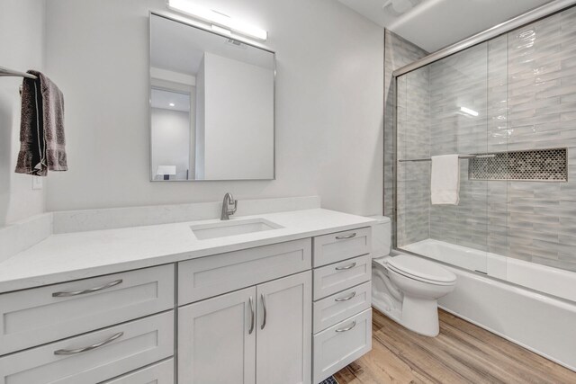 full bathroom with vanity with extensive cabinet space, toilet, shower / bath combination with glass door, and hardwood / wood-style floors