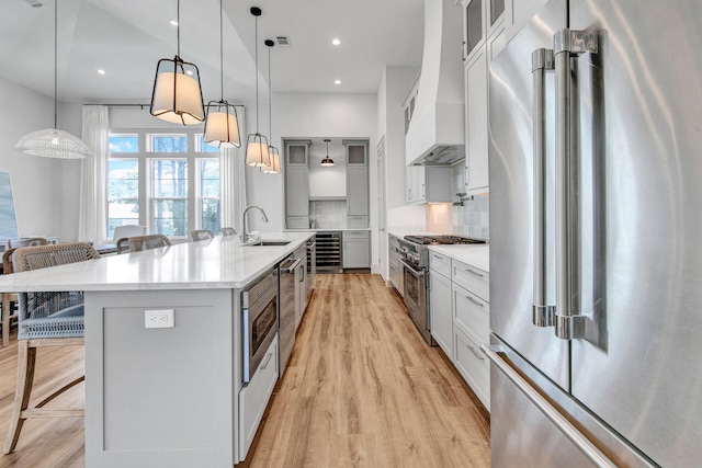 kitchen with sink, high quality appliances, backsplash, a center island with sink, and custom range hood