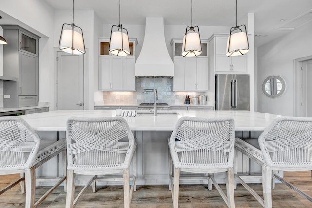 kitchen featuring appliances with stainless steel finishes, backsplash, custom range hood, hardwood / wood-style floors, and pendant lighting