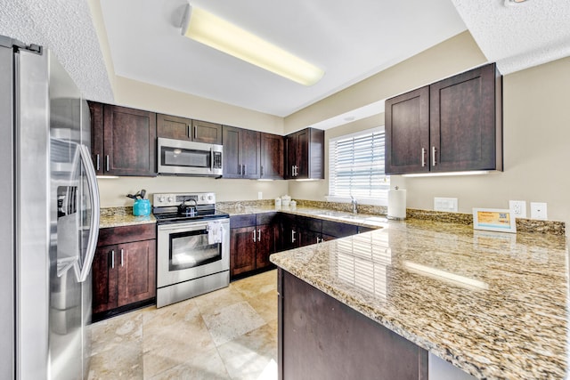 kitchen with dark brown cabinets, light stone countertops, appliances with stainless steel finishes, sink, and light tile floors