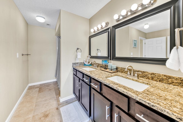 bathroom featuring a textured ceiling, vanity with extensive cabinet space, double sink, and tile flooring