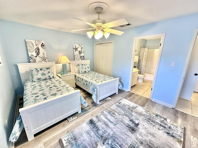 bedroom with ceiling fan, light hardwood / wood-style floors, ensuite bath, and a closet