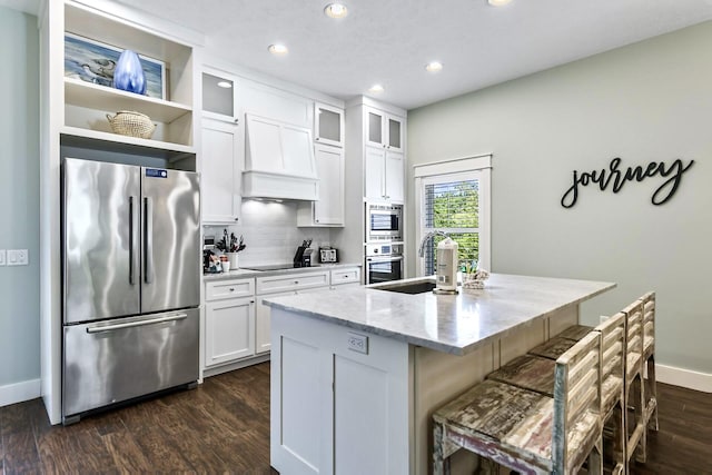 kitchen with white cabinetry, sink, stainless steel appliances, custom range hood, and a center island with sink