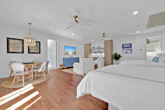 bedroom with ceiling fan with notable chandelier, hardwood / wood-style floors, and wood walls