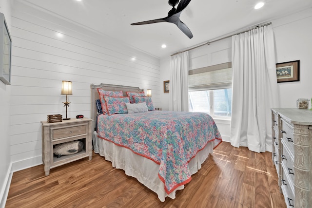 bedroom with hardwood / wood-style floors, ceiling fan, and wood walls