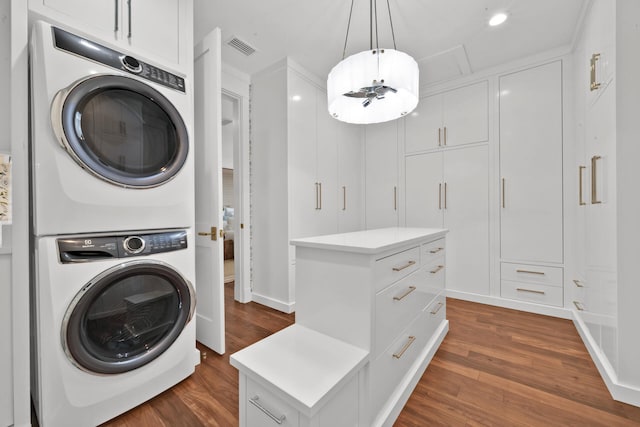 laundry room featuring stacked washer / dryer, dark hardwood / wood-style floors, and cabinets