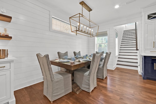 dining room featuring dark hardwood / wood-style floors, a notable chandelier, and wooden walls