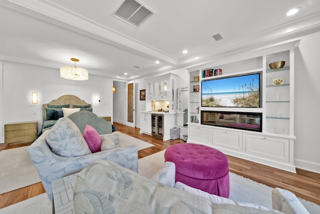 living room featuring crown molding, bar area, built in features, beverage cooler, and light hardwood / wood-style floors