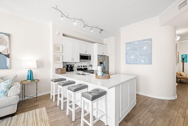 kitchen featuring backsplash, a breakfast bar, kitchen peninsula, white cabinetry, and stainless steel appliances