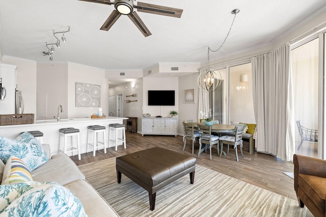 living room featuring light wood-type flooring, a textured ceiling, crown molding, ceiling fan with notable chandelier, and sink