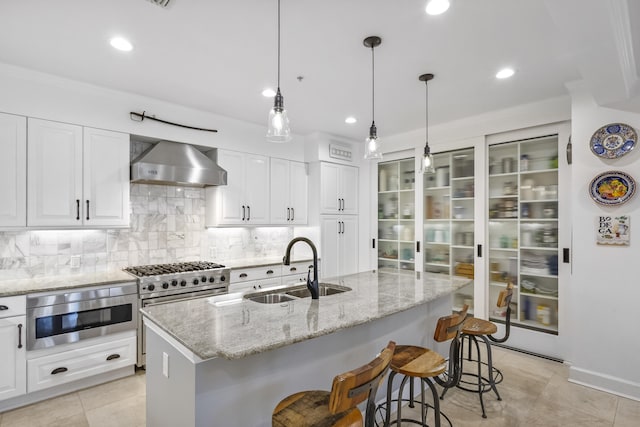 kitchen with sink, light tile patterned floors, oven, an island with sink, and wall chimney exhaust hood