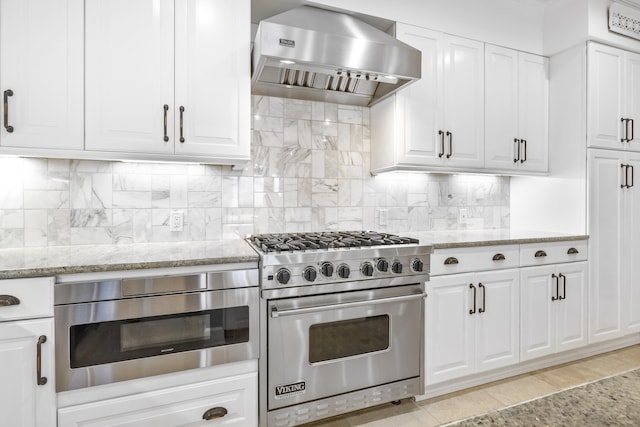 kitchen with appliances with stainless steel finishes, light stone countertops, decorative backsplash, and wall chimney exhaust hood