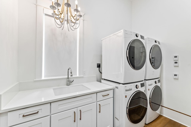 laundry room featuring stacked washer and dryer, sink, a notable chandelier, light hardwood / wood-style floors, and cabinets