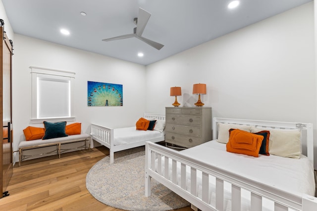 bedroom featuring light hardwood / wood-style flooring, ceiling fan, and a barn door