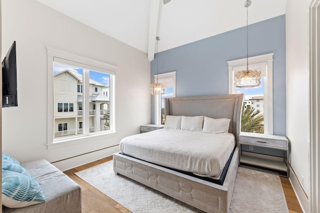 bedroom with lofted ceiling with beams, a notable chandelier, and light hardwood / wood-style flooring