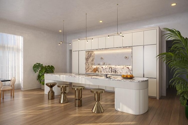 interior space featuring light wood-type flooring, decorative light fixtures, white cabinets, and light stone countertops