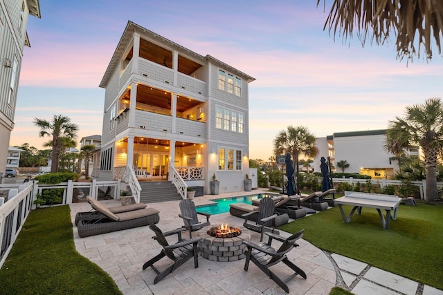 back house at dusk featuring a patio, a fire pit, a lawn, and a balcony