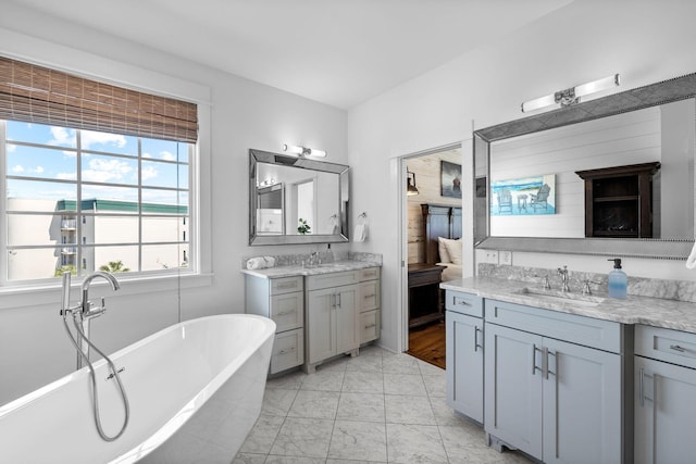 bathroom with a washtub, double sink vanity, tile floors, and a wealth of natural light