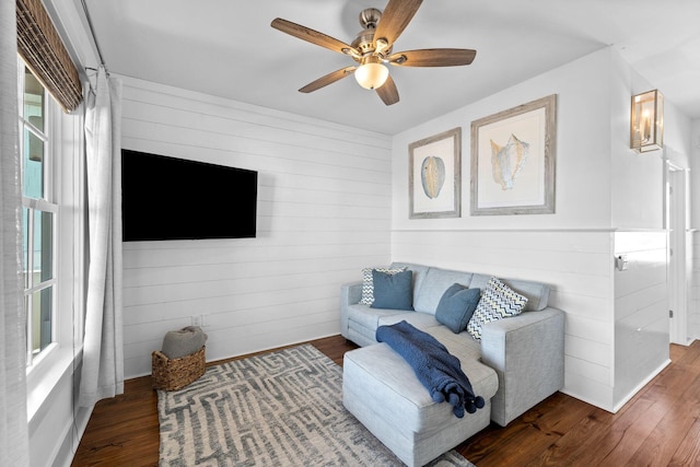 living room with dark hardwood / wood-style flooring, ceiling fan, and wood walls