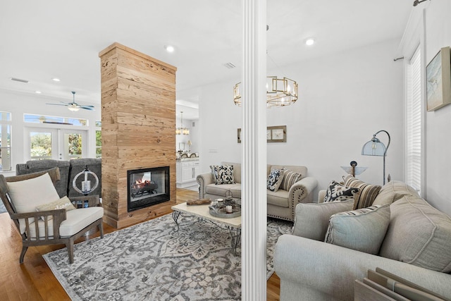 living room featuring wood-type flooring, ceiling fan with notable chandelier, and a tiled fireplace